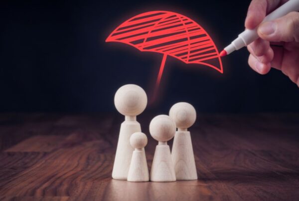 A hand drawing a red umbrella over a group of wooden figures, representing family protection and the importance of verifying roofing contractor insurance.